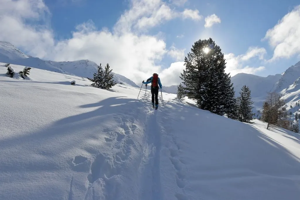 skitouren geher beim aufstieg durch pulverschnee, im hintergrund bergekulisse in oberbayern bei sonnenschein