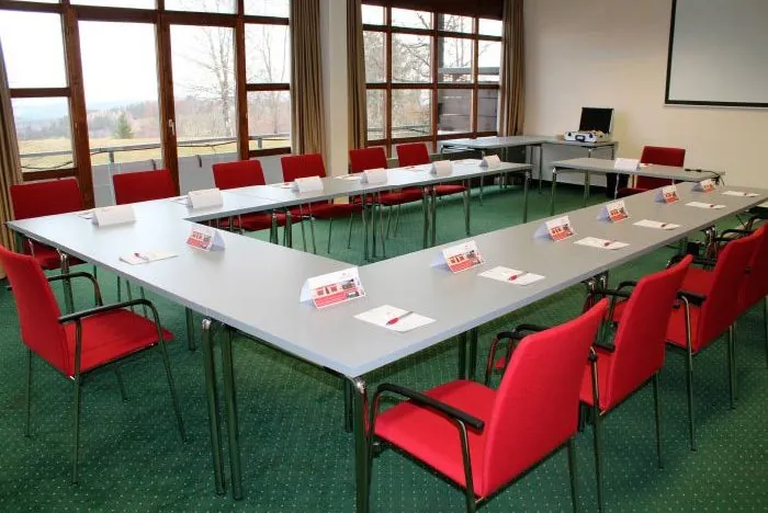 Seminarraum in U-Form mit Namensschildern, Schreibblöcken, Beamer und großer Fensterfront mit Blick ins Grüne